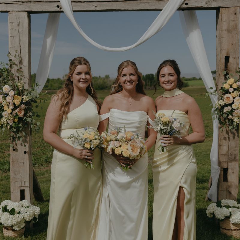 Bride and two bridesmaids with floral arbor decor in the background